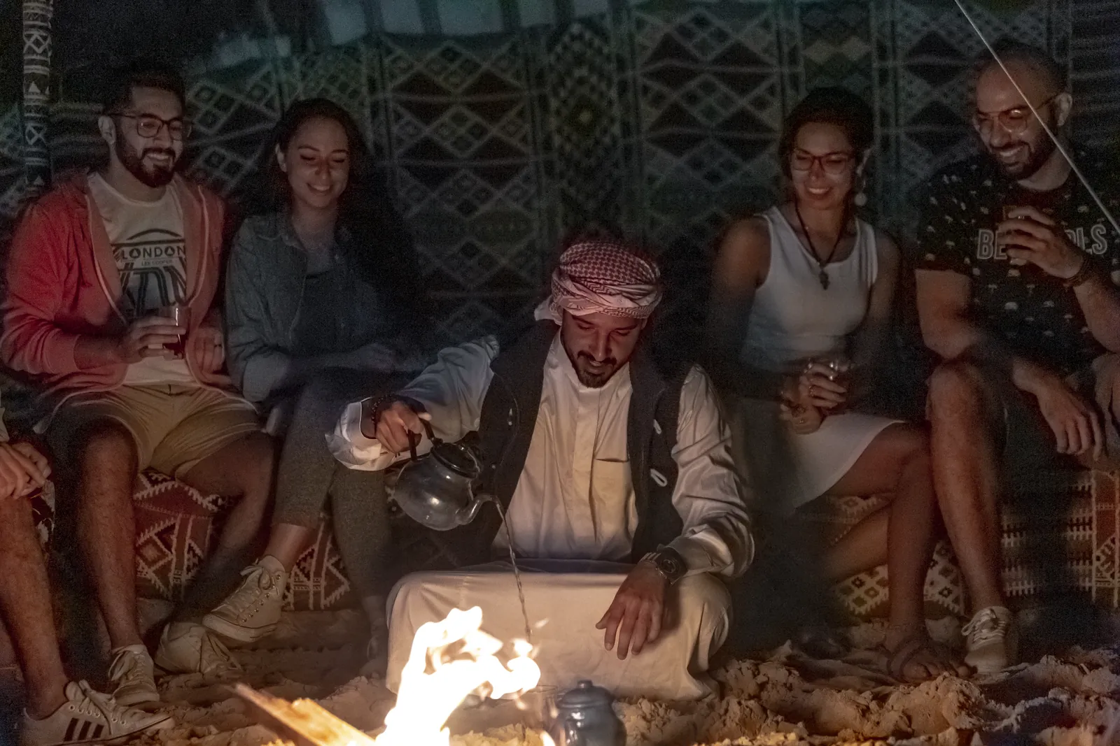 أصدقاء يضحكون حول نار المخيم ليلاً