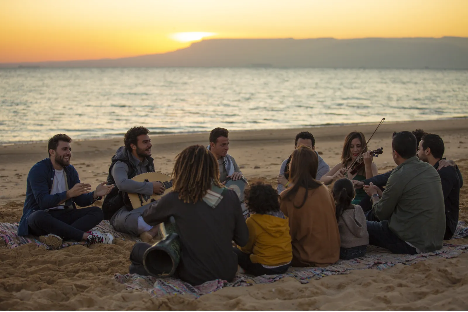 Friends playing music on the beach at sunset